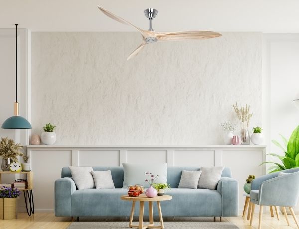 Ventilateur de plafond silencieux à trois pales en bois, monté au centre d’un salon lumineux avec canapé bleu et plantes décoratives.