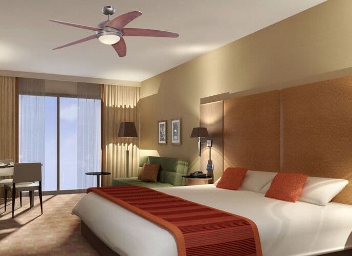 Ventilateur de plafond moderne dans une chambre d'hôtel, au-dessus d’un grand lit, avec lumière douce et décor chaleureux. ventilateur plafond consommation électrique intégrée naturelle dans la description.