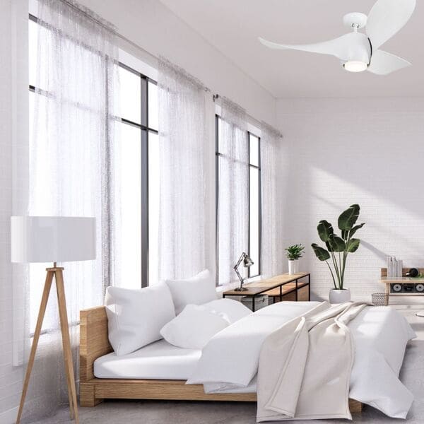 Ventilateur de plafond blanc au-dessus d’un lit dans une chambre lumineuse, ambiance calme et moderne. Comment régler le ventilateur plafond pour optimiser la vitesse et sens de rotation.