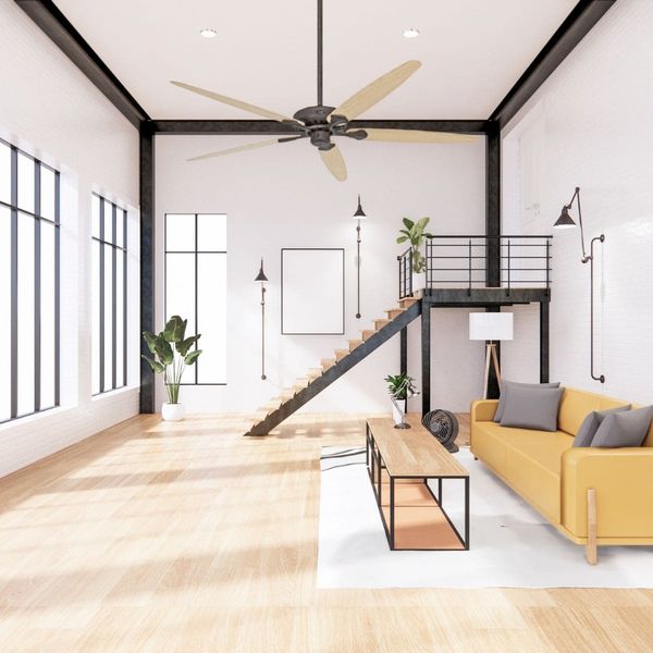 Salon spacieux au style moderne avec ventilateur de plafond allumé au centre, canapés jaune et table basse, mezzanine et escalier noir, grande luminosité naturelle.