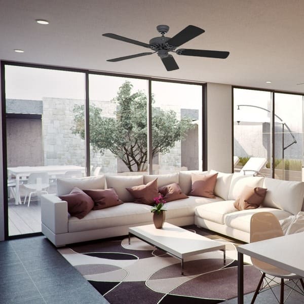 Ventilateur de plafond noir à quatres pales installé dans un séjour moderne avec canapés blancs et grandes fenêtres.