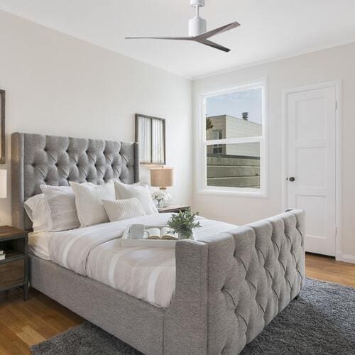 Une chambre lumineuse avec un lit à baldaquin gris et un ventilateur de plafond moderne au-dessus.