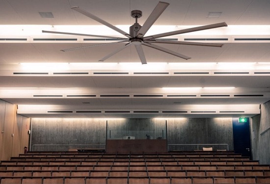 Salle de conférence vide avec de grandes rangées de sièges et un ventilateur mural au plafond.