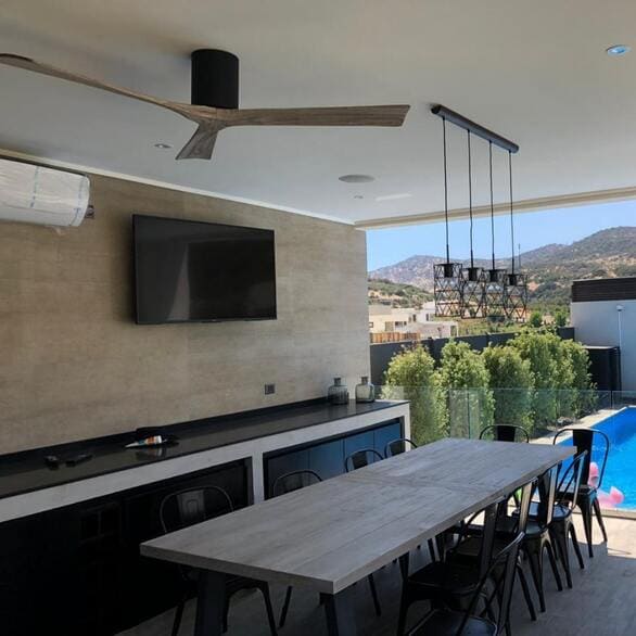 Terrasse extérieure aménagée avec une table longue et des chaises, vue sur la piscine et les collines.