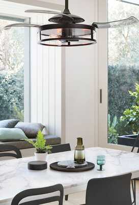 Le ventilateur est suspendu au plafond au-dessus d’une table, avec la grille et les pales visibles.