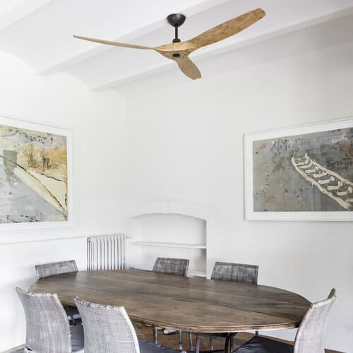 Ventilateur de plafond à trois pales au-dessus d’une grande table ronde dans une salle blanche.