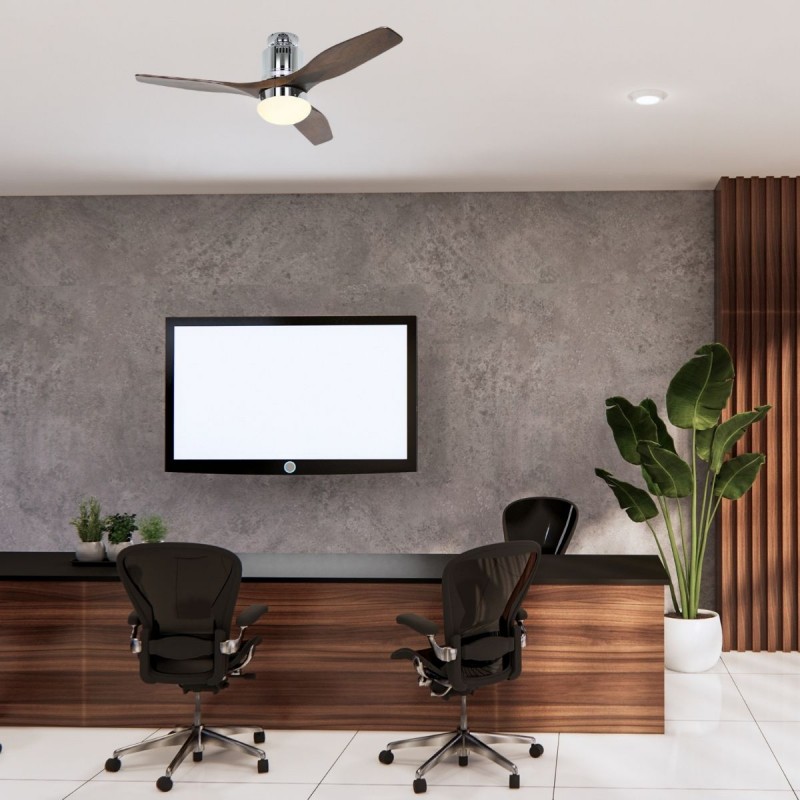 Ventilateur de plafond au-dessus d’un espace de travail avec deux fauteuils autour d’un bureau, écran mural et plante verte